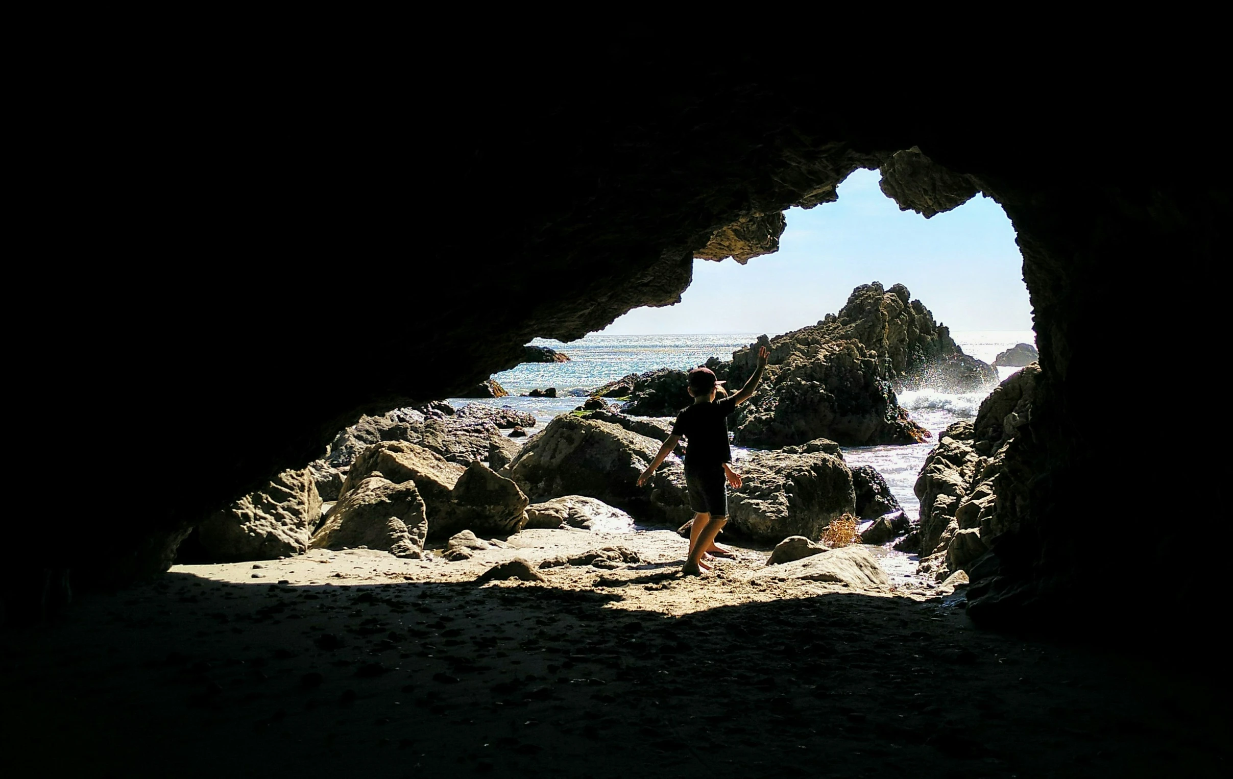 a woman standing under a dark cave near a beach