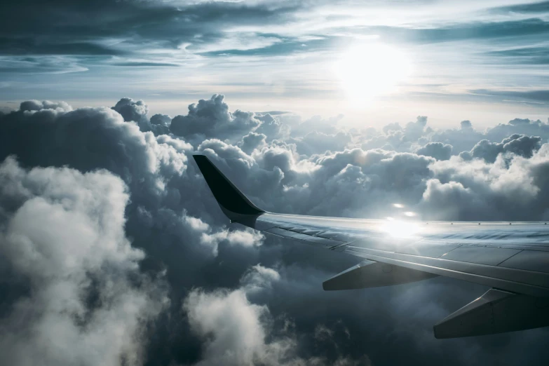 view of the wing of an airplane with sun peeking through the clouds