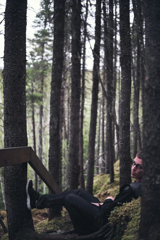 a man with glasses laying in the woods