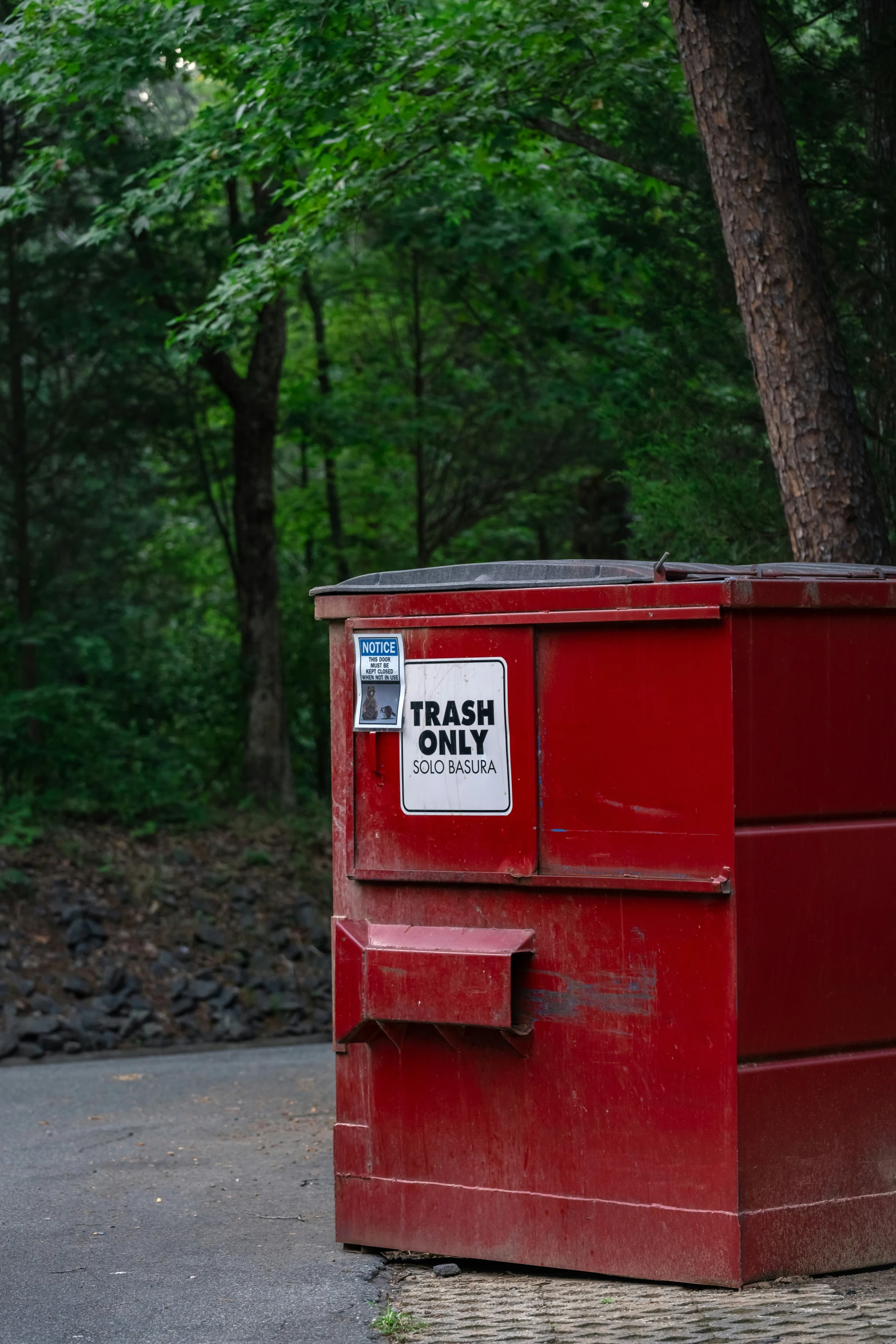 a red trash bin sitting in front of a tree