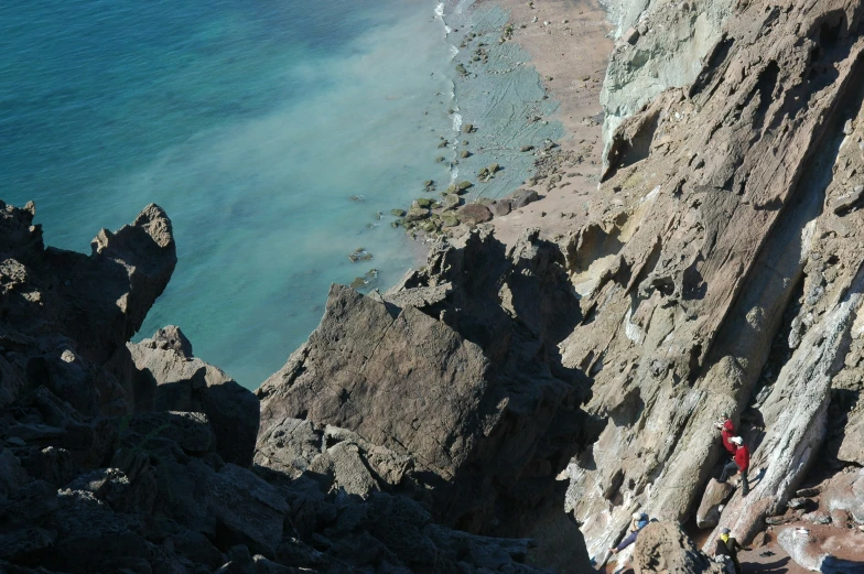 a hiker climbing up to the side of a rocky cliff by the ocean
