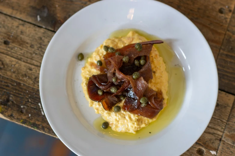 a plate with hummus, bacon and capers on it