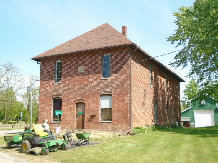 people work on a lawn with an old house in the background