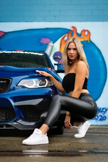 a woman sits on the ground next to a blue bmw