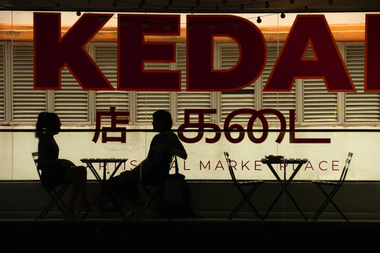 two people sitting on chairs next to a sign that reads keda