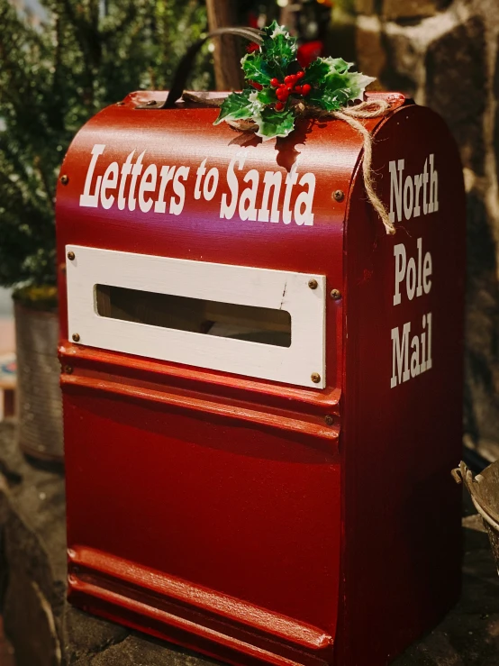 a post box with a red ribbon on top and letters to santa written in white writing on it