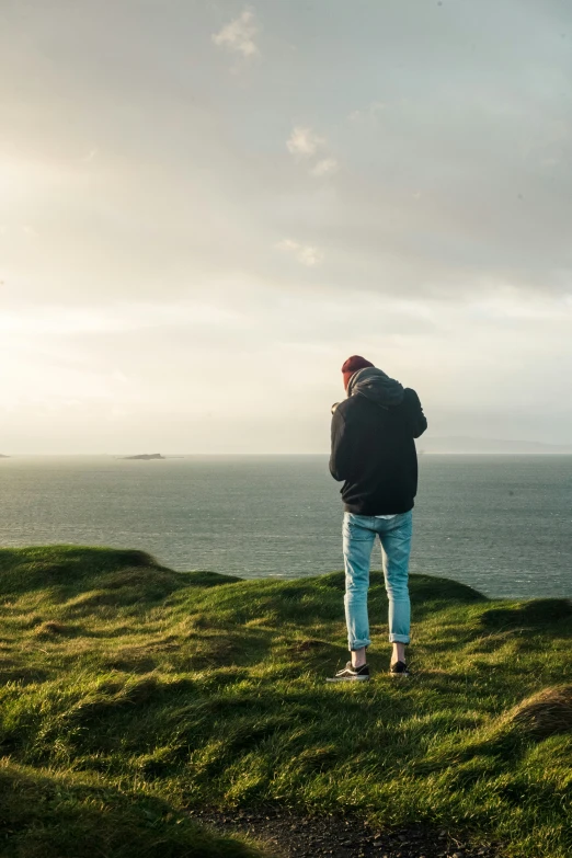 a man in blue jeans standing on top of a hill