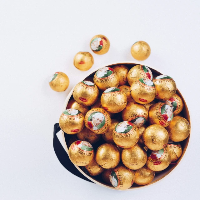 gold - colored chocolate eggs in a metal container with a white background