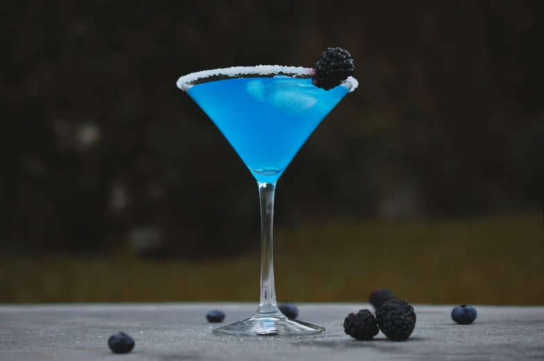 an empty martini glass with blue colored liquid and blackberries on it