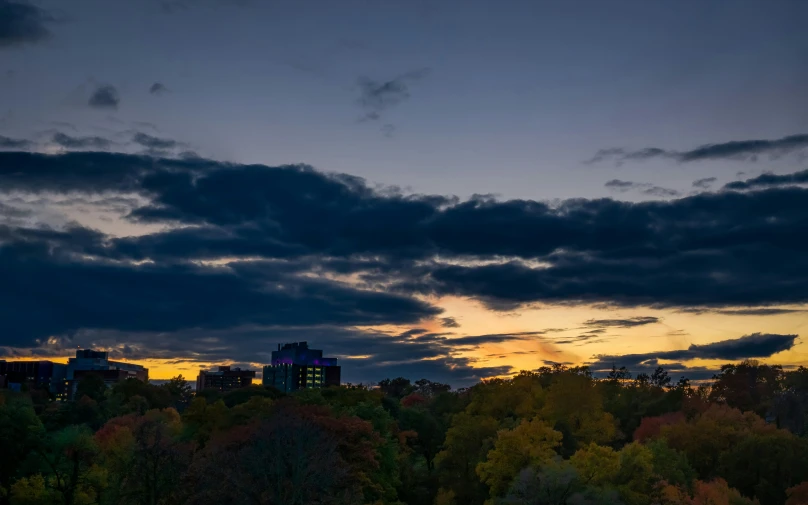 the sun is setting in a cloudy sky over trees