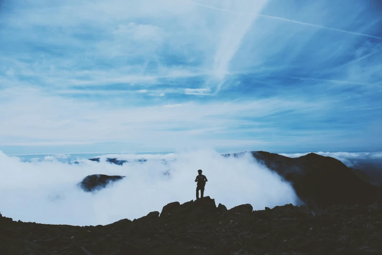 a person stands on a rocky outcropping above the clouds