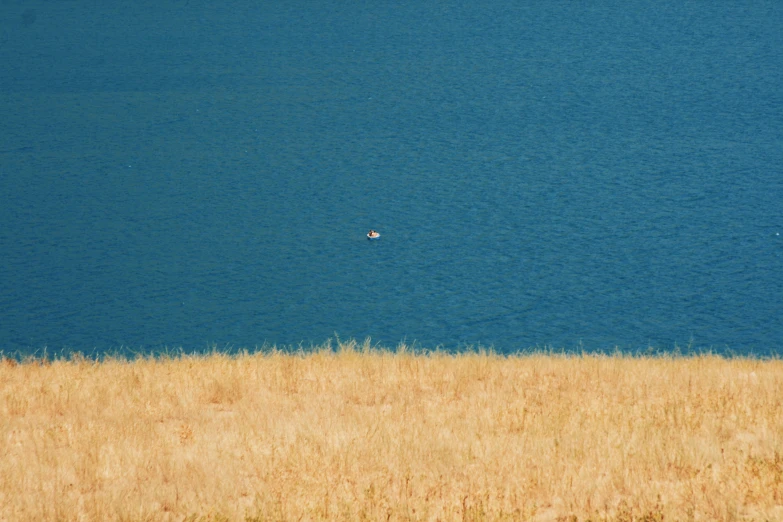 a lone boat floats on the water from a dry grass field