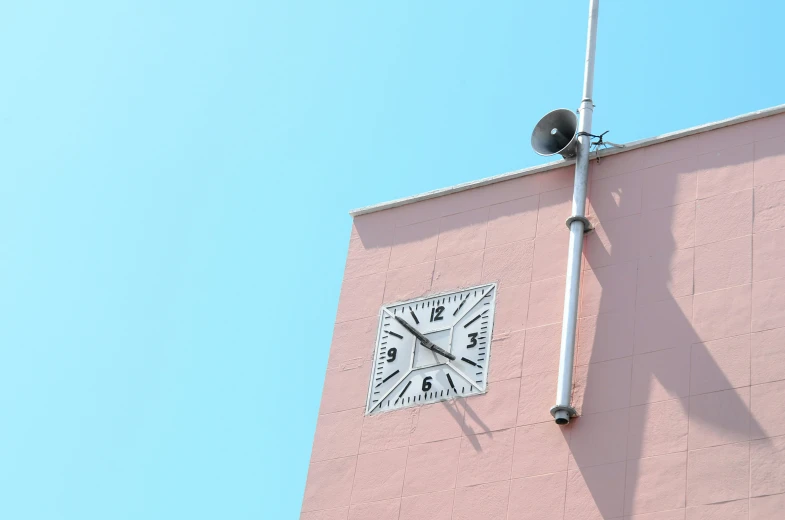 a square clock on the side of a pink building