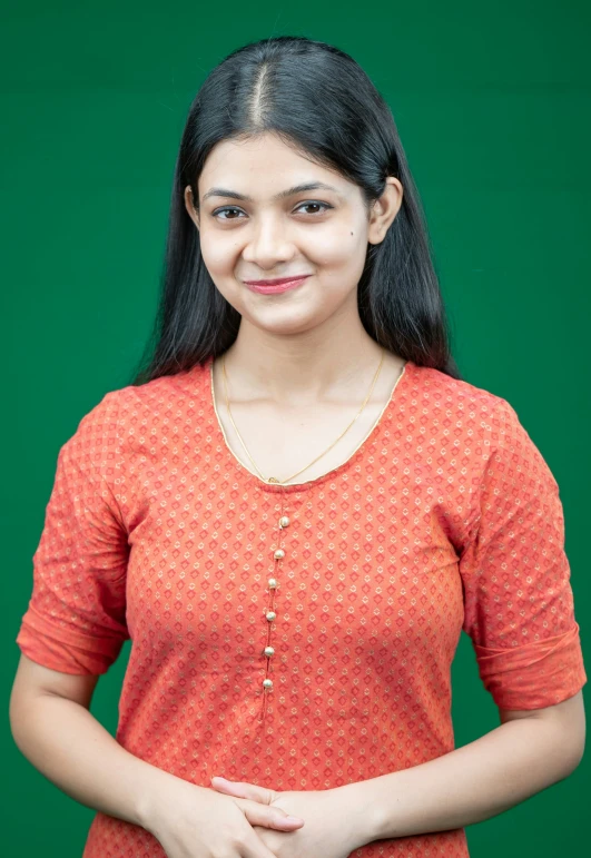 a girl standing in front of a green background wearing an orange top