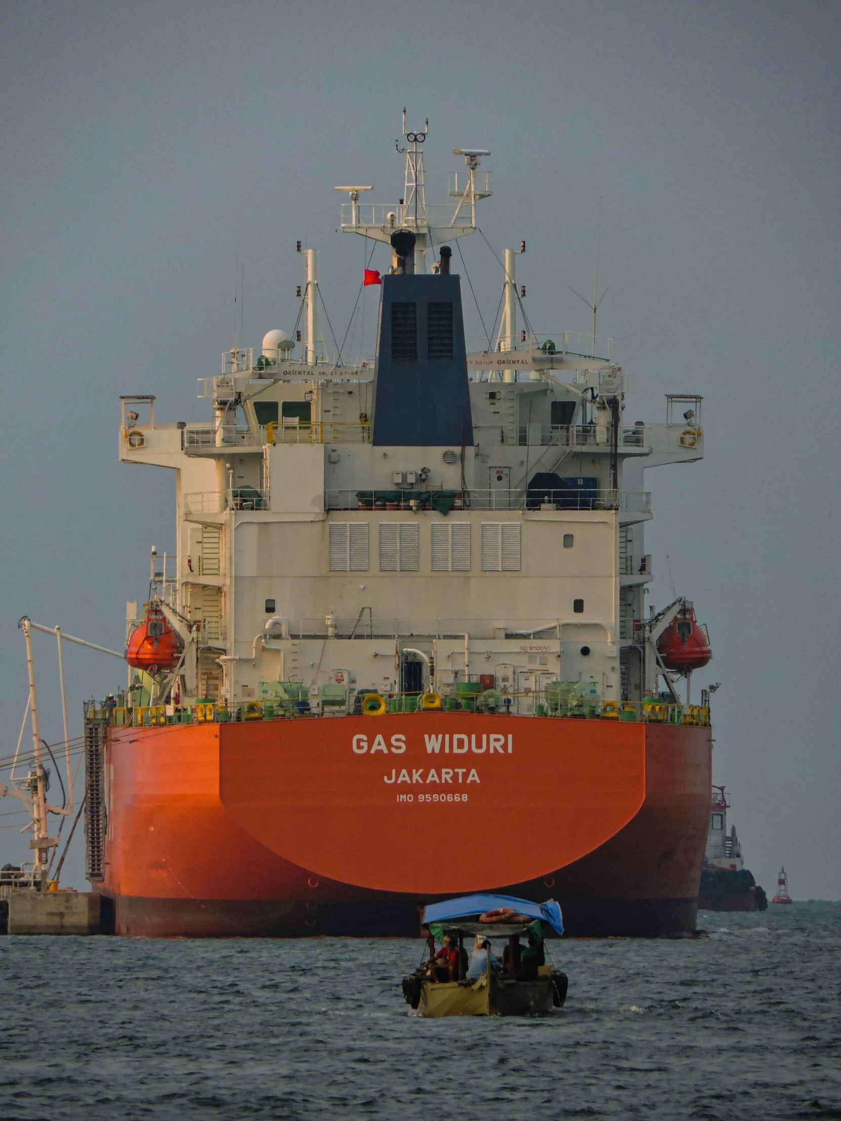 a tug boat travels past a big orange ship