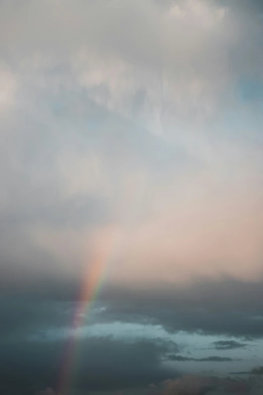 a rainbow and dark cloudy skies above a hill