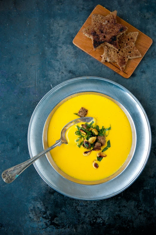 a bowl of carrot soup on a table with toast and other foods