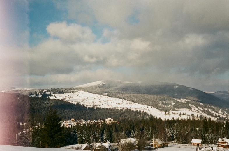 an open field covered in snow with mountains and houses in the distance