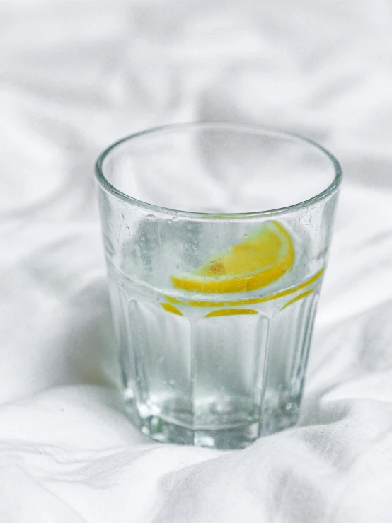 a glass of water with water and lemon slice on a table cloth