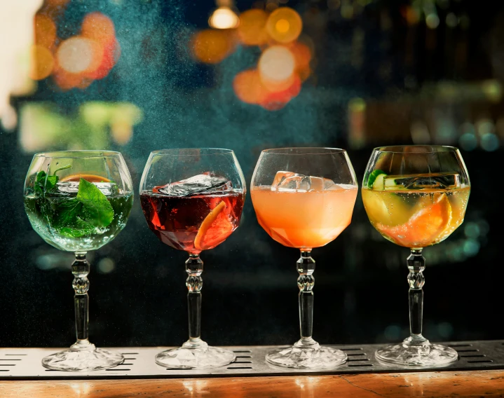 five glasses of various cocktails sitting on a bar