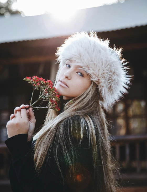a woman is wearing a winter hat while holding flowers