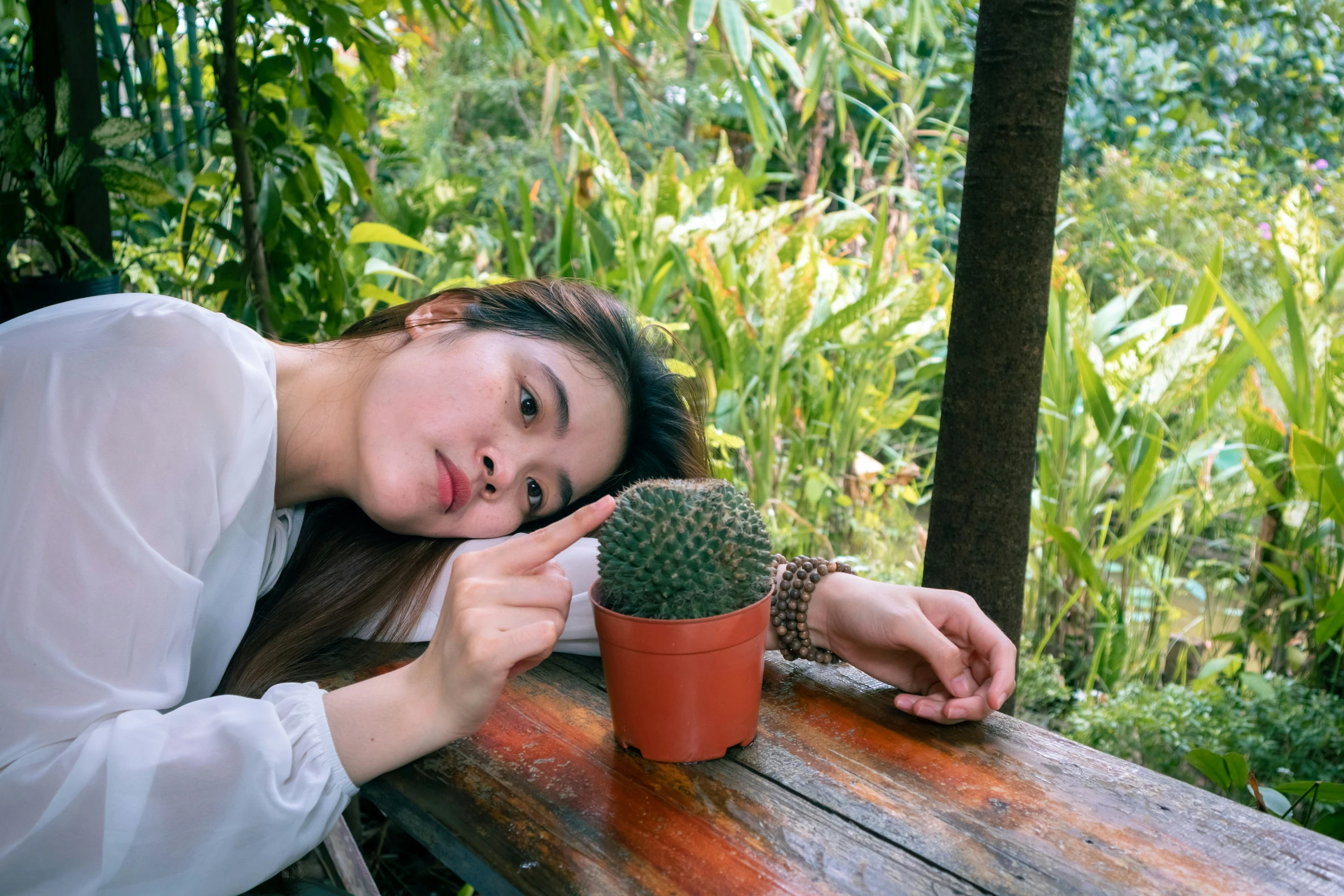 a beautiful young lady sitting on top of a wooden table next to a potted cactus