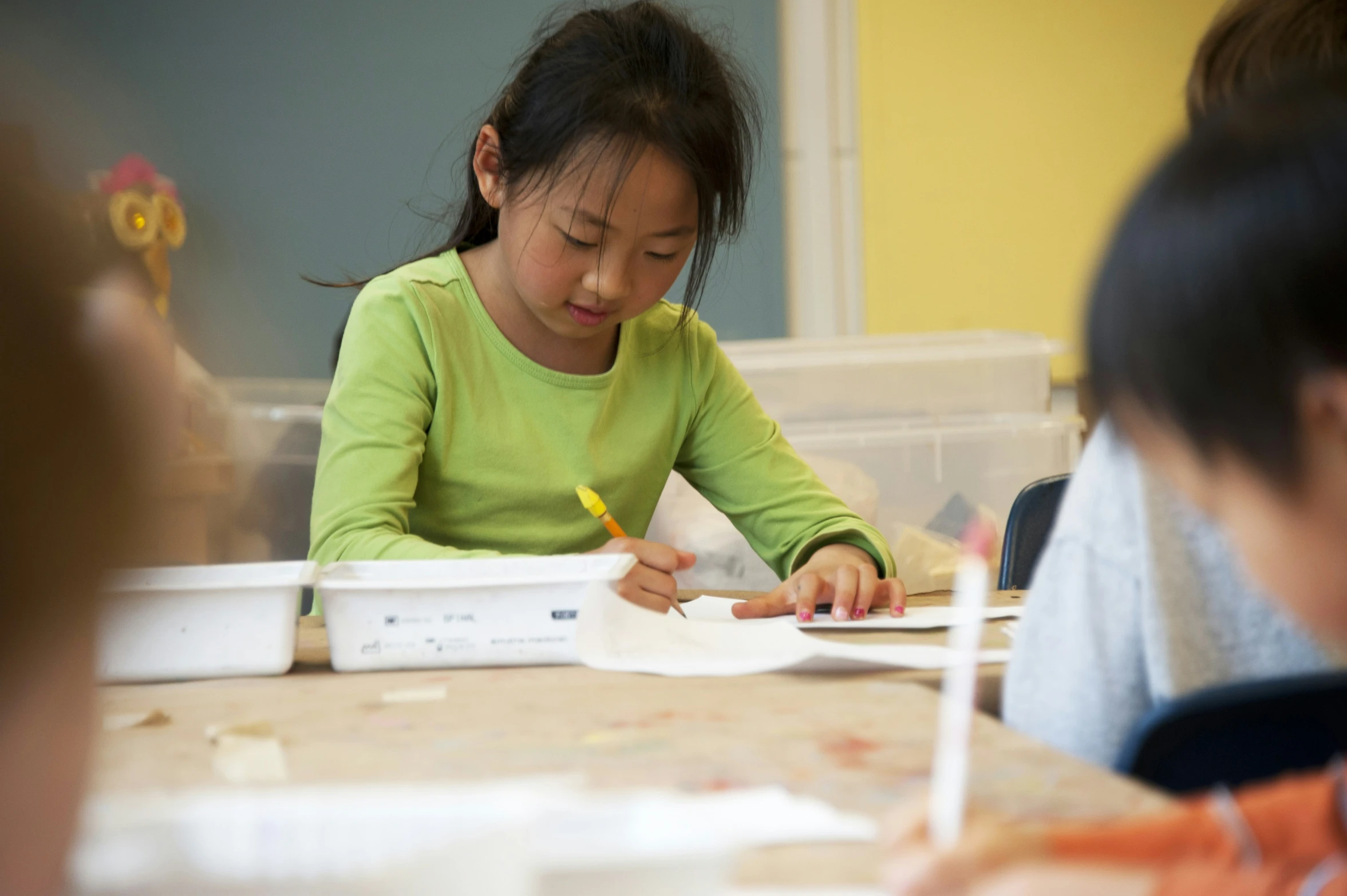 a girl is sitting at a table writing on paper