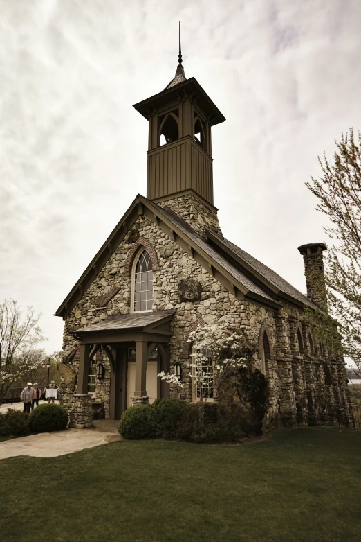 a stone church with a steeple on it in front of grass and trees