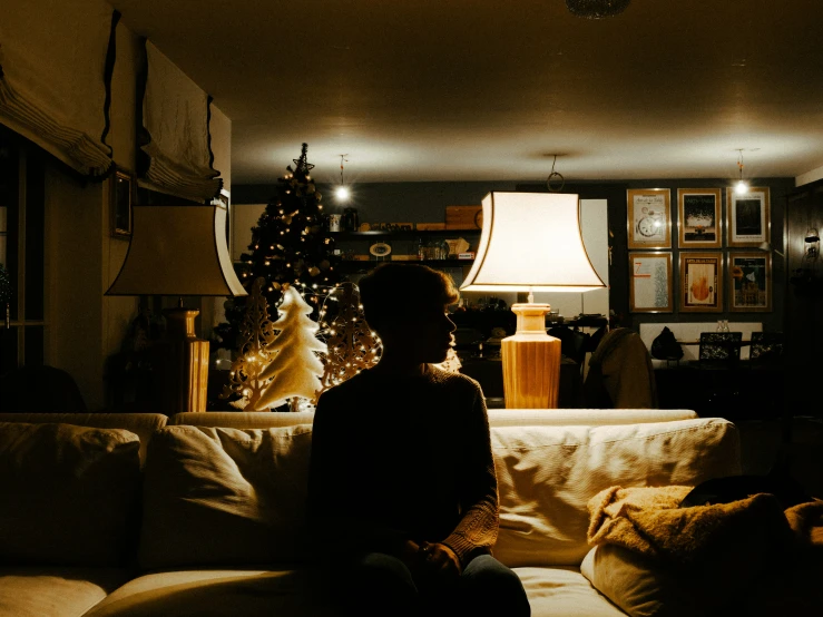 a black and white pograph of a person sitting on a couch near christmas trees