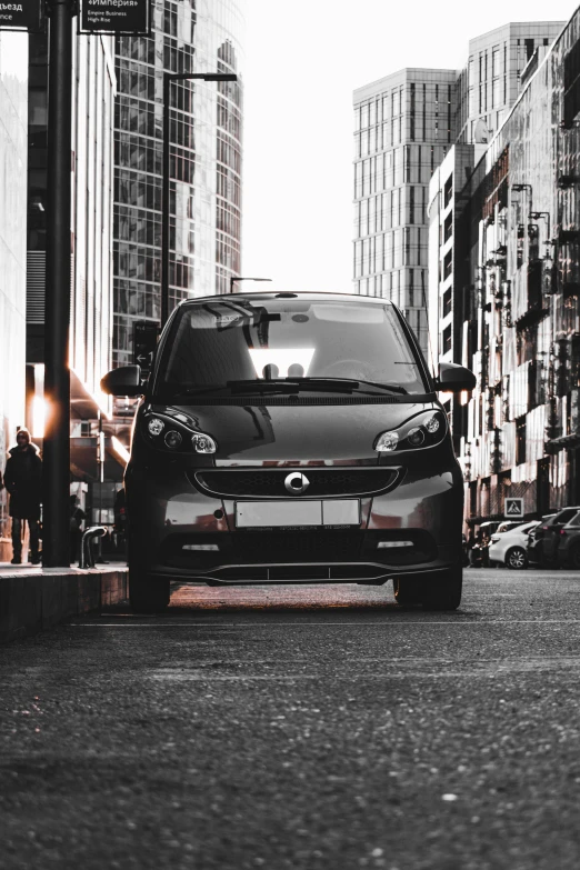 a small car driving down a street past tall buildings