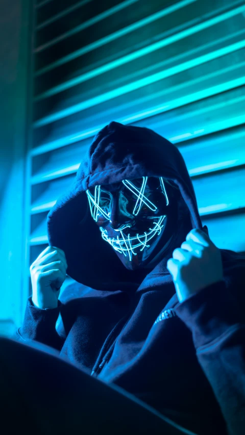 a person in a hooded hoodie with a neon mask on and a black background