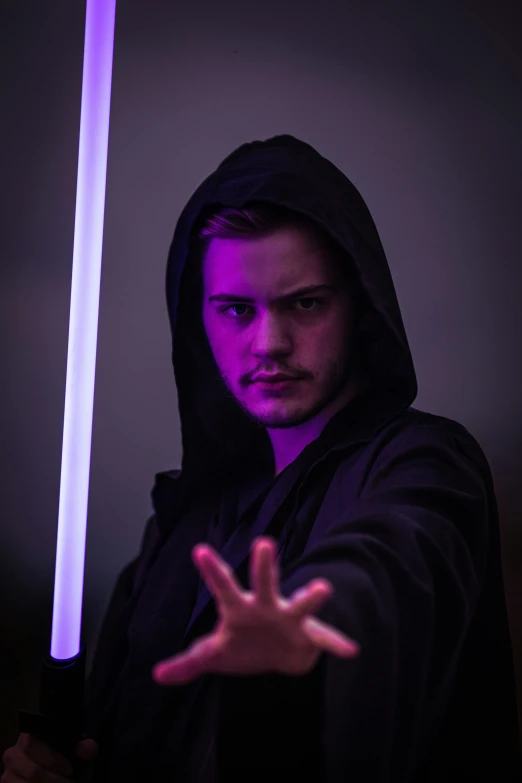 a man with long hair and a hooded jacket is holding a purple light saber