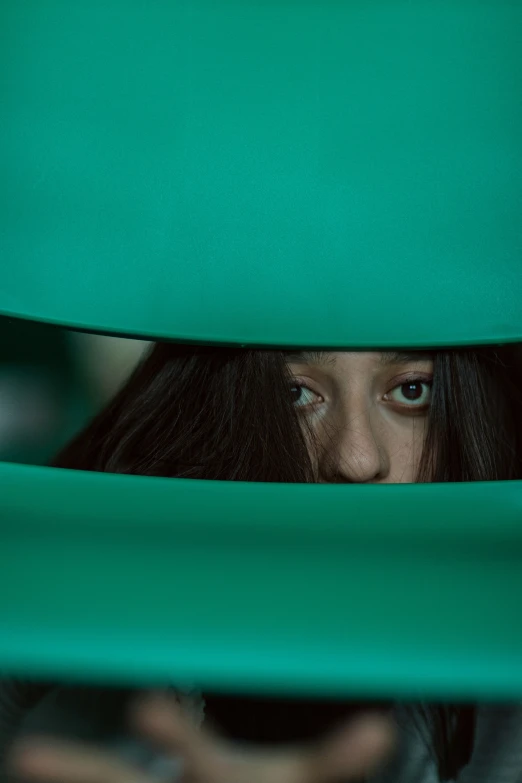 a woman peeks through the green fabric behind her