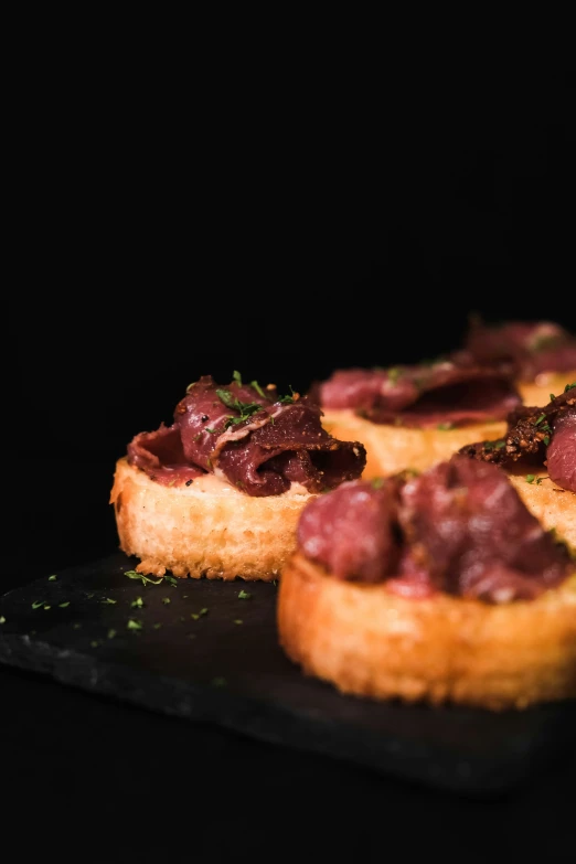 small appetizers with meat and bread on a black plate