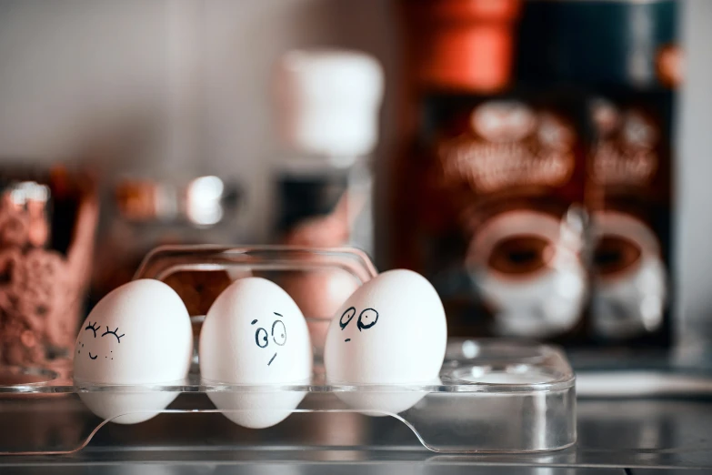 an egg tray with three white eggs and the faces drawn on them