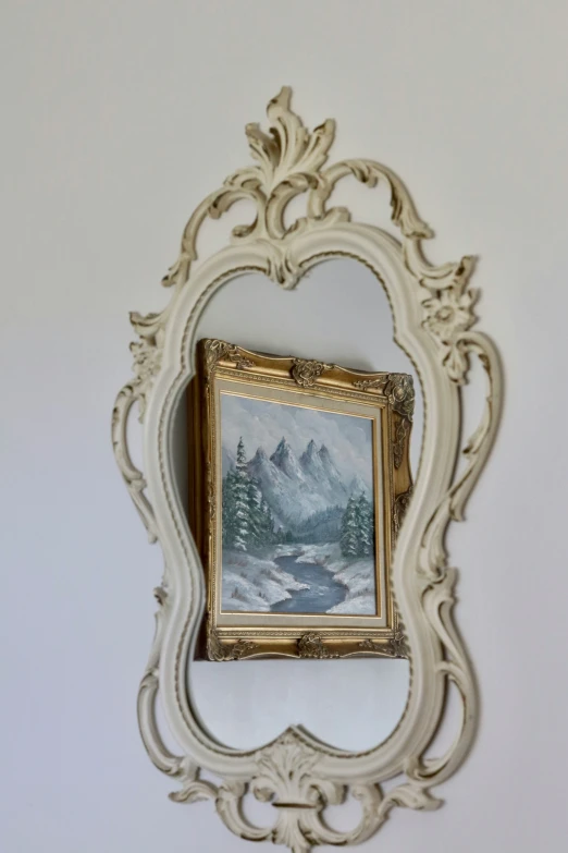 the framed painting depicts a snowy scene as the border is decorated with gold and wood