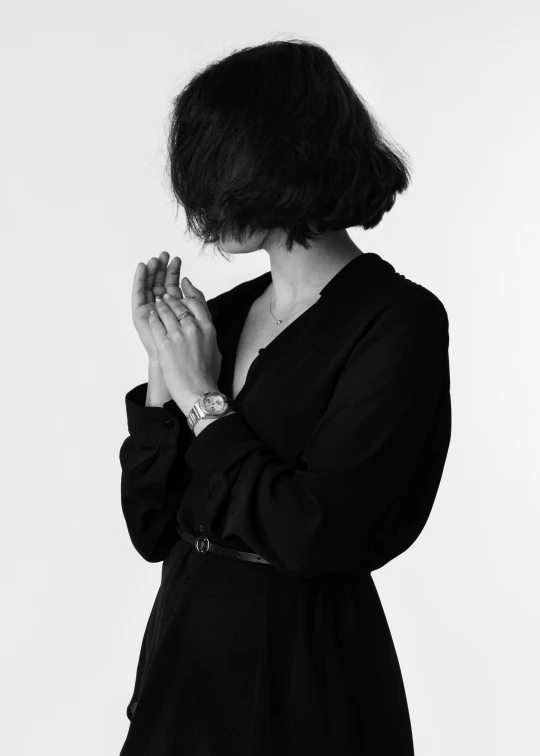 a woman wearing an unoned black dress standing with her hands folded around her