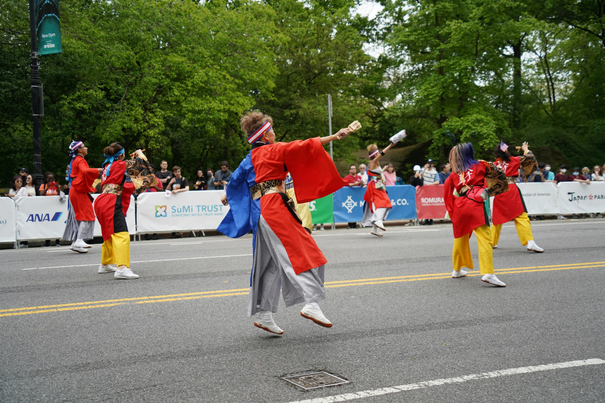 dancers performing in a street parade with trees and a fence