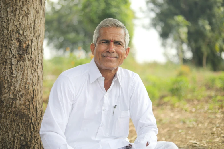 an indian man in white sitting under a tree