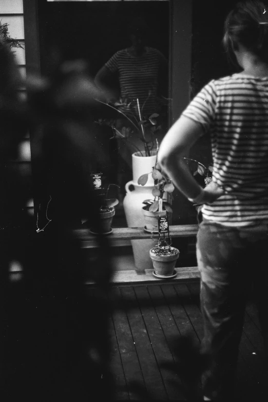 the black and white po shows a woman standing at her own side with potted plants in the kitchen