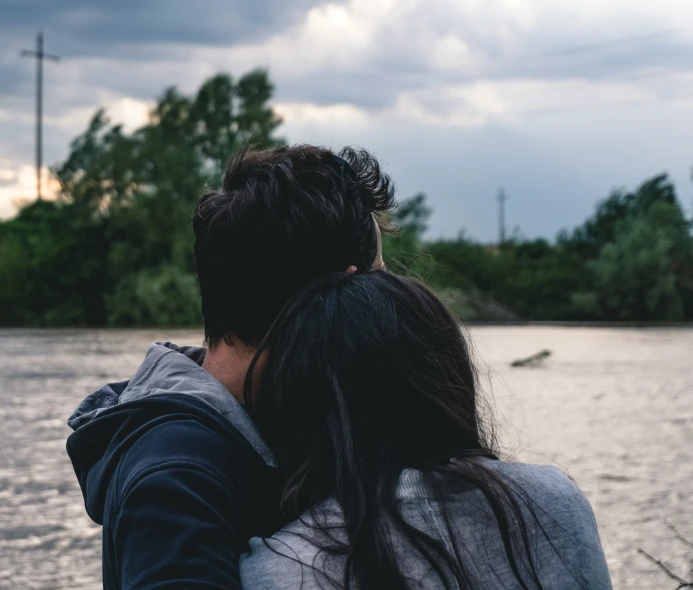 a man and woman hugging in front of the water