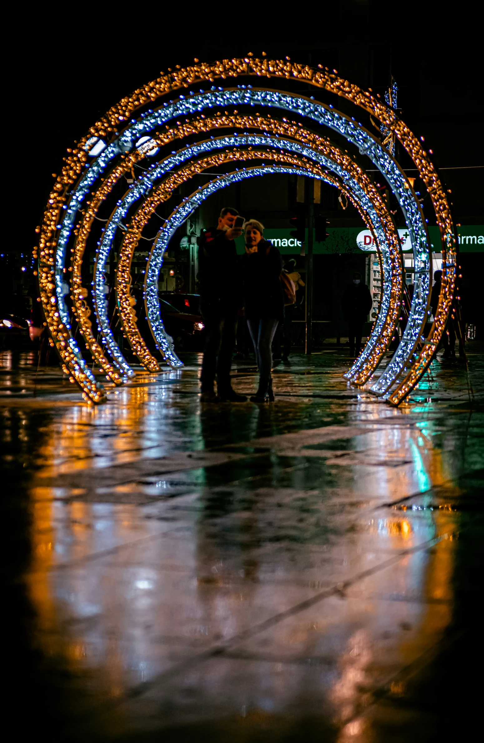 two people standing under a colorfully lit christmas arch