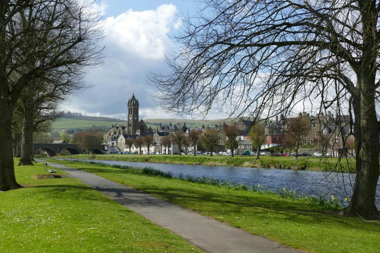 a pathway near a water way with buildings and a clock tower in the background