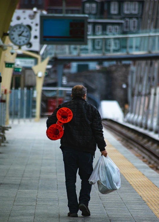 the man carrying two bags of red poppies is walking along the train tracks