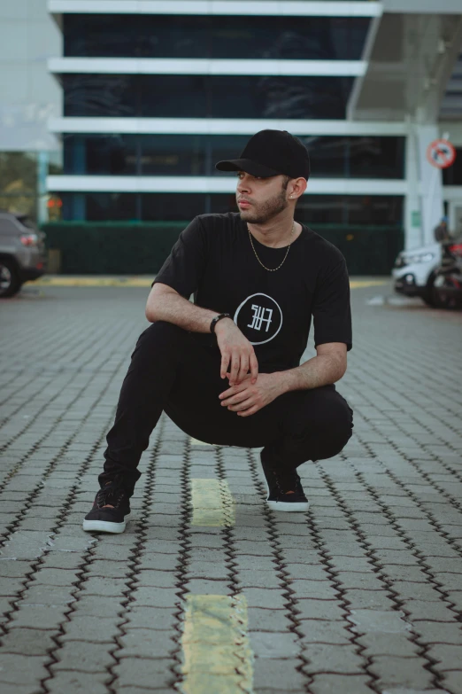 a man in black shirt crouches on a brick walkway