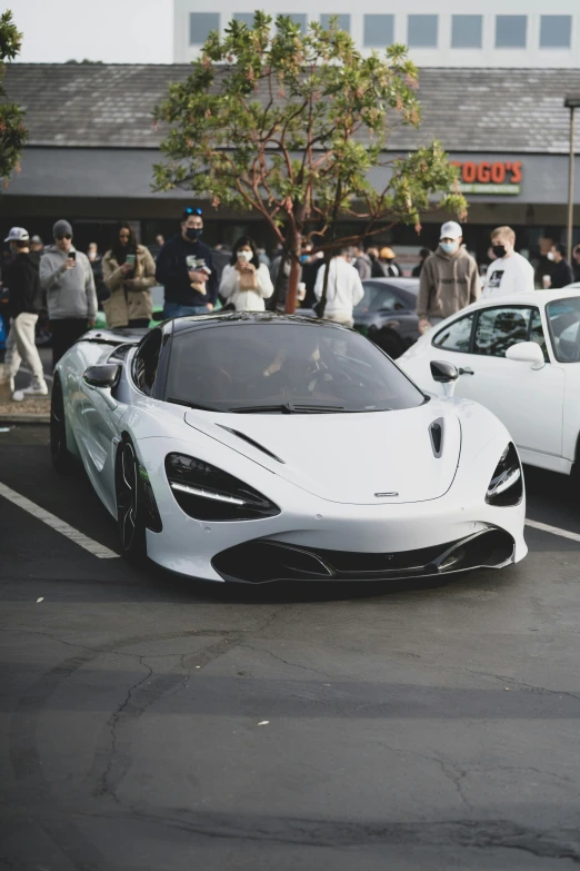 some people standing in line and looking at two expensive sports cars