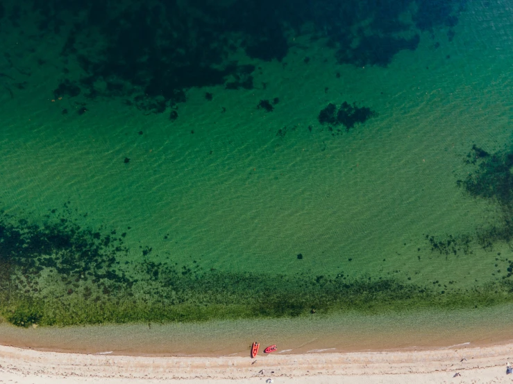 an aerial view of a sandy beach with two people in the water