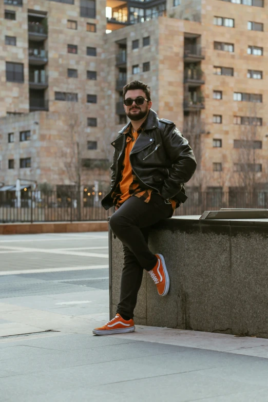 a man is sitting on a ledge with a leather jacket on