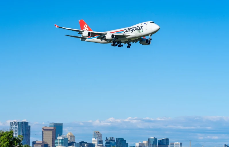 a white and blue airplane flying in the sky over city skyline