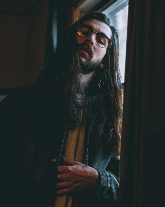 a man with long hair standing in front of a window